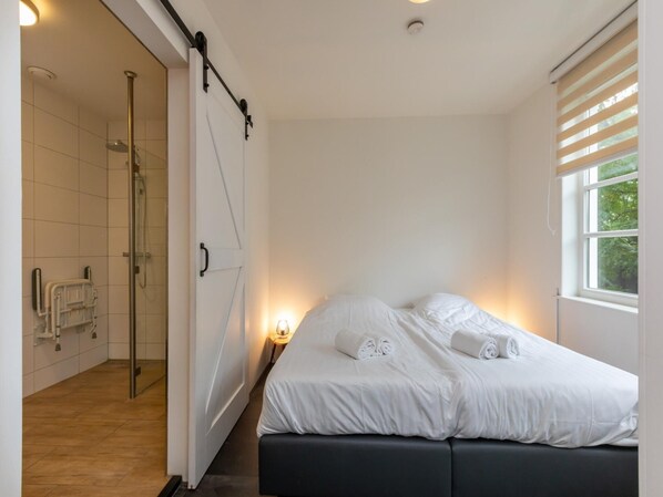 A bedroom with a bed, a window, and a shower area.