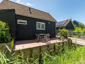 Ein Holzhaus mit einem Ziegeldach, einer Terrasse mit Tisch und Stühlen sowie ein Garten mit Pflanzen.