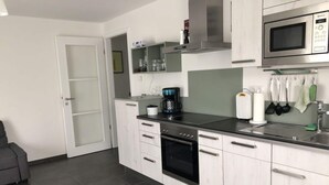 A modern kitchen with white cabinetry, a black countertop, a built-in oven, a microwave, and a coffee maker. - Holiday Apartment Meadow (Sulzburg)