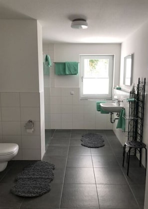 A bathroom with a toilet, sink, and a window. There are two rugs on the floor. - Holiday Apartment Meadow (Sulzburg)