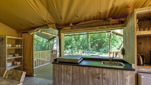 A rustic wooden cabin with a kitchen area featuring a sink, a wooden counter, and a window overlooking a forested area.