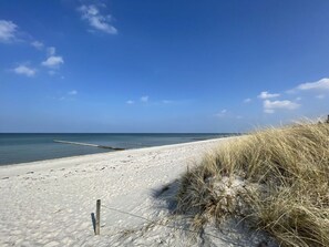 Una playa arenosa con un poste de madera y hierba a la derecha.