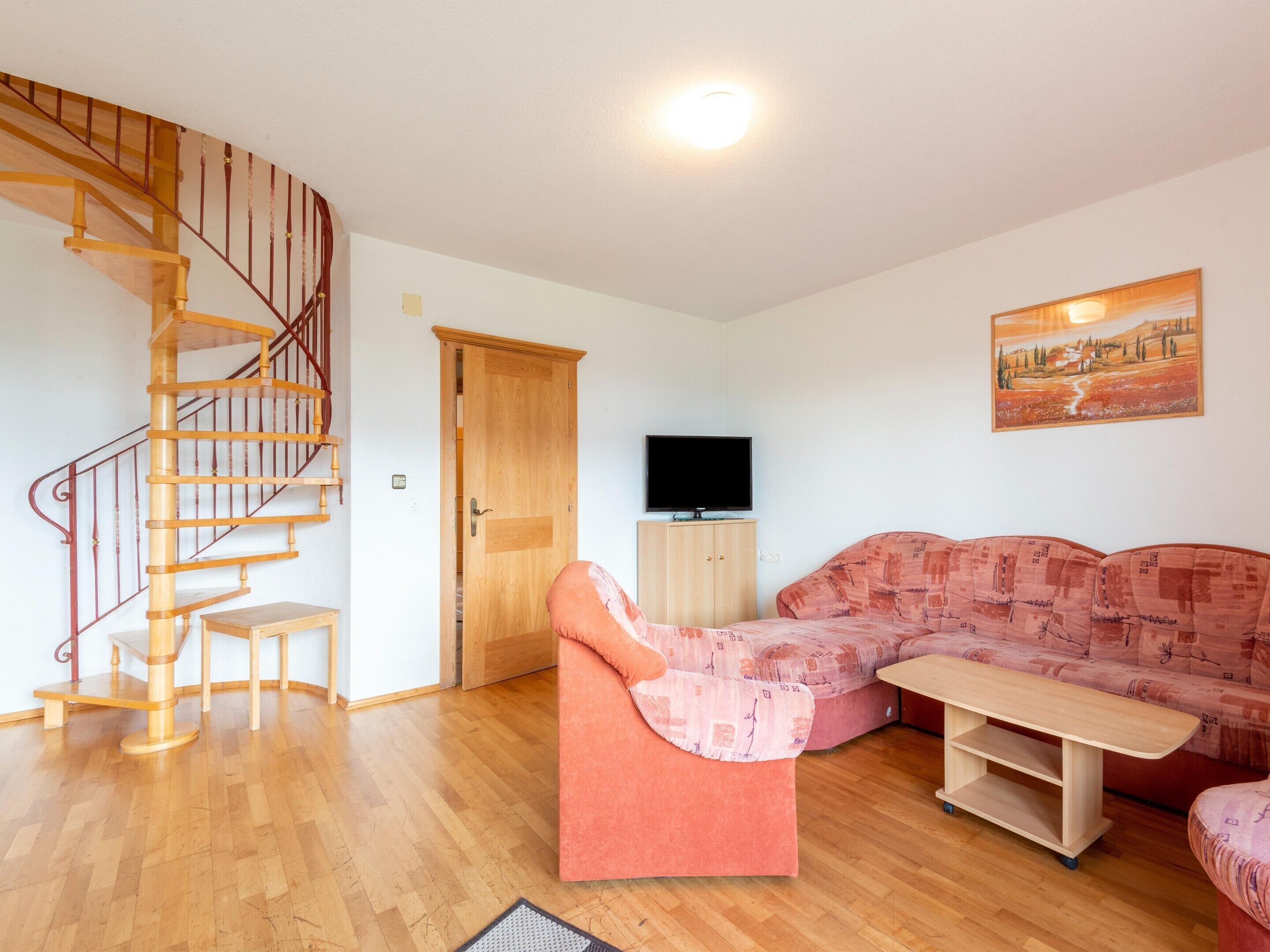Een woonkamer met een houten trap, een bank, een televisie en een schilderij aan de muur.