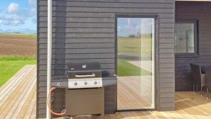 A barbecue grill on a wooden deck with a view of a grassy field. - 12 Person Holiday Home in Lemvig (Lemvig)