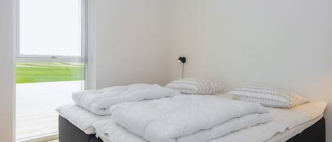 A bedroom with a large bed, a window, and a wall-mounted light.