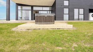 A modern house with a hot tub on a wooden deck, large windows, and a covered patio area. - 12 Person Holiday Home in Lemvig (Lemvig)