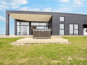 A modern house with a hot tub on a wooden deck, large windows, and a covered patio area. - 12 Person Holiday Home in Lemvig (Lemvig)