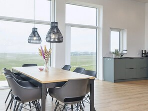 Un espace de repas moderne avec une table et des chaises en bois, de grandes fenêtres et une vue sur l’extérieur.