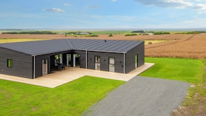 A modern house with a flat roof, a covered patio, and a view of the surrounding fields. - 12 Person Holiday Home in Lemvig (Lemvig)