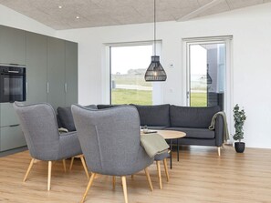 En moderne stue med en grå sofa, to lænestole, et lille rundt bord og en hængende lampe.