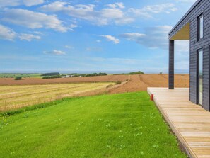 Un bâtiment moderne doté d’une terrasse en bois qui offre une vue sur une pelouse verdoyante et des champs.