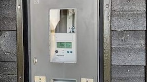 A utility meter with a digital display, mounted on a grey metal door with a wooden panel background. - 12 Person Holiday Home in Lemvig (Lemvig)