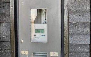A utility meter with a digital display, mounted on a grey metal door with a wooden panel background. - 12 Person Holiday Home in Lemvig (Lemvig)