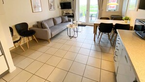 A modern living room with a sofa, chairs, a dining table, and a kitchen area with a TV and oven. - 4 Person Holiday Home in Hadsund (Hadsund)