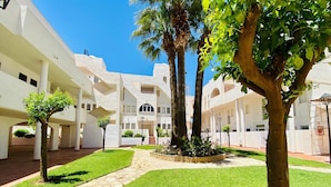 A courtyard with white buildings, palm trees, and a stone pathway. - Belvilla by OYO Aldea Marina (Garrucha)