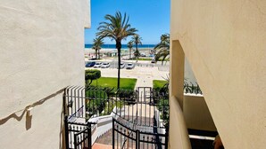 A balcony with a view of a beach, palm trees, and parked cars. - Belvilla by OYO Aldea Marina (Garrucha)