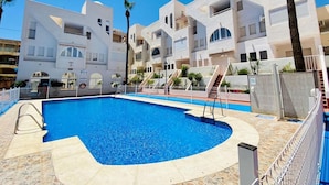 A swimming pool surrounded by modern buildings with balconies and a clear blue sky. - Belvilla by OYO Aldea Marina (Garrucha)