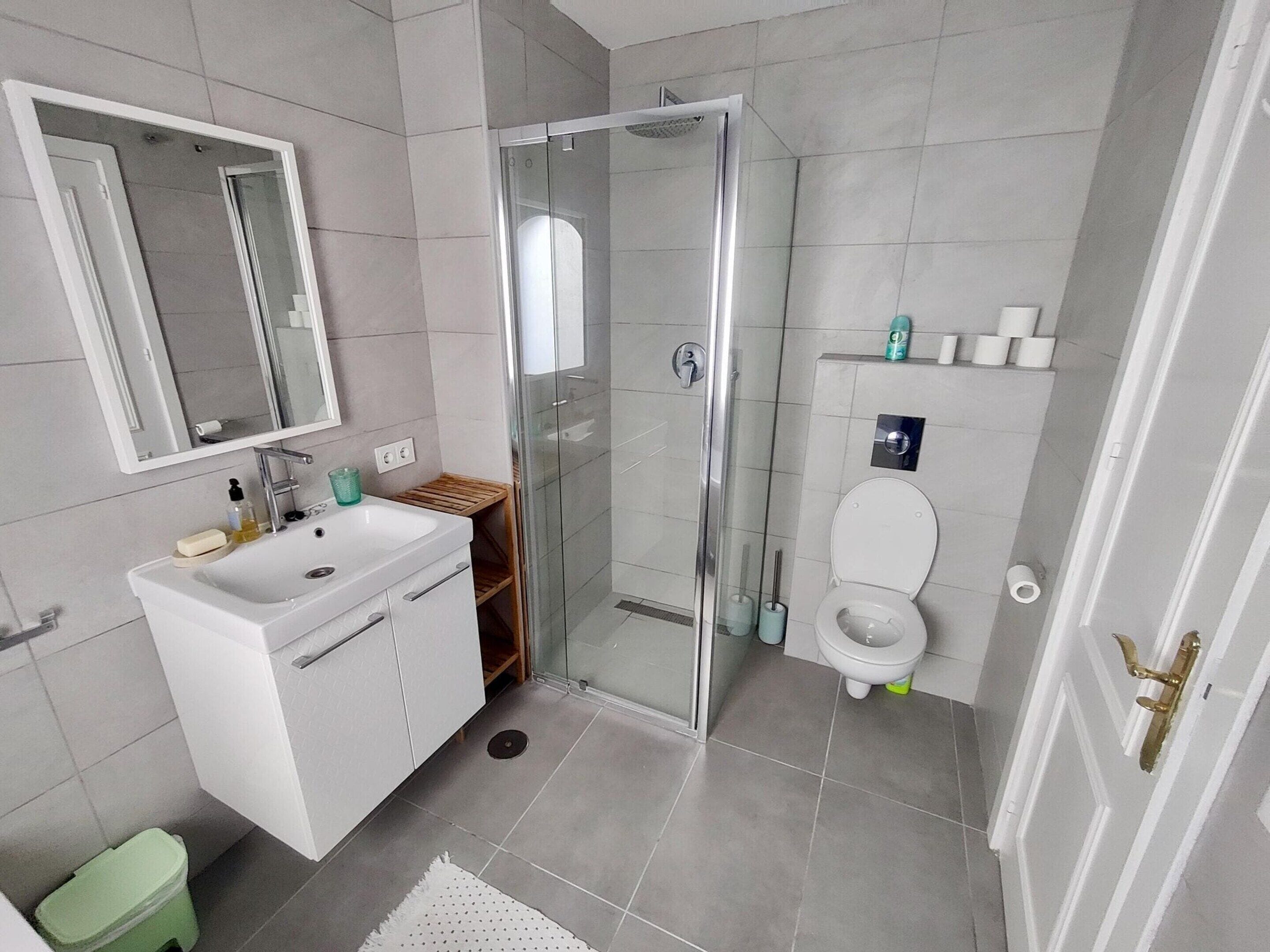 A modern bathroom with a glass-enclosed shower, a white sink, and a toilet.