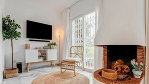 A living room with a TV, a fireplace, a wicker chair, and a large window.