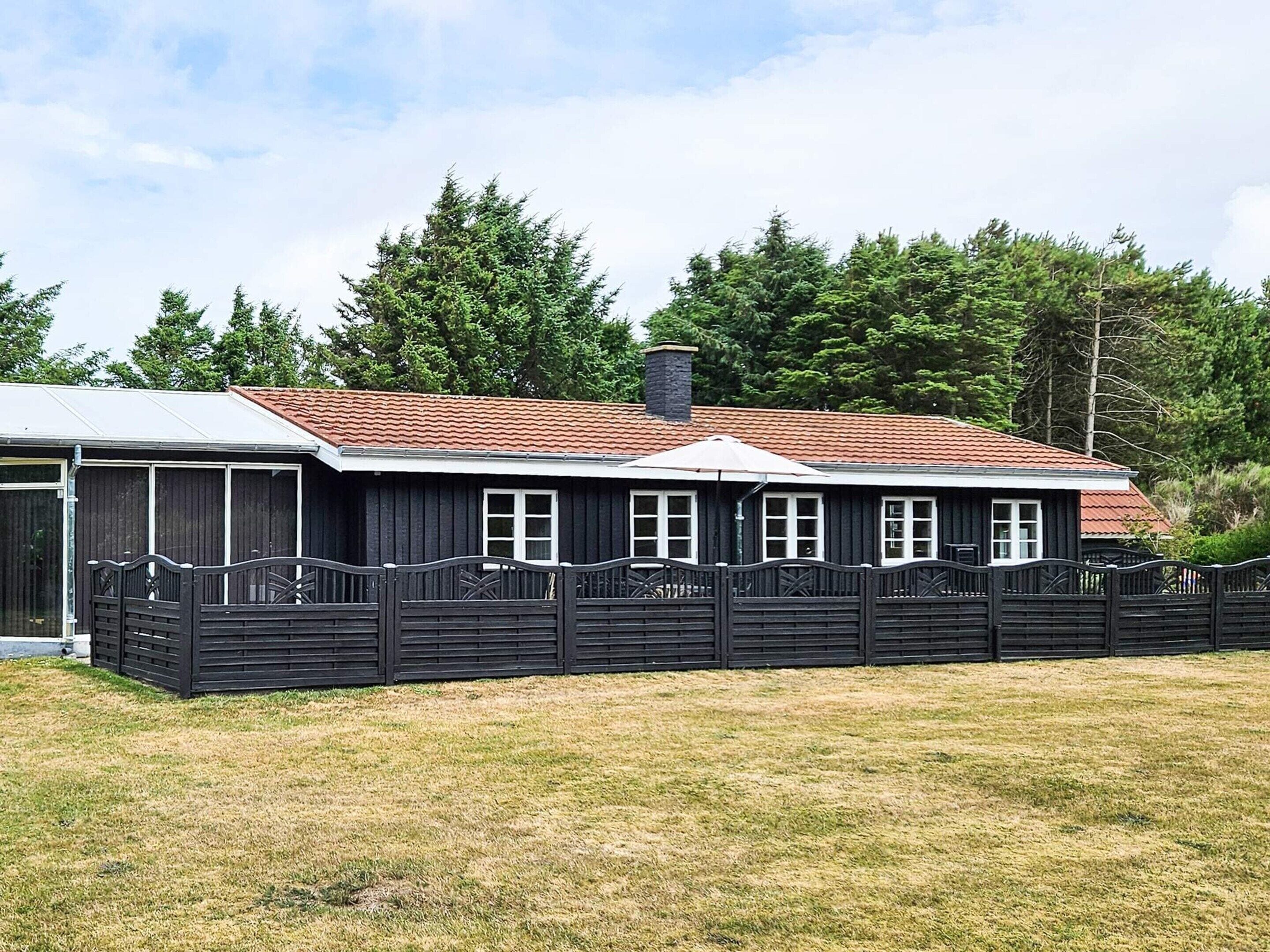 A two-story building with a red-tiled roof, a fenced area, and a grassy field in front.