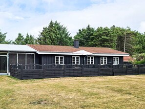 Un bâtiment à deux étages, doté d’un toit recouvert de tuiles rouges, d’une zone délimitée par une clôture et d’un terrain herbeux à l’avant.