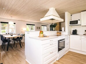A modern kitchen with white cabinetry, a central island, a built-in oven, and a microwave. - 4 Star Holiday Home in Lokken (Lokken)