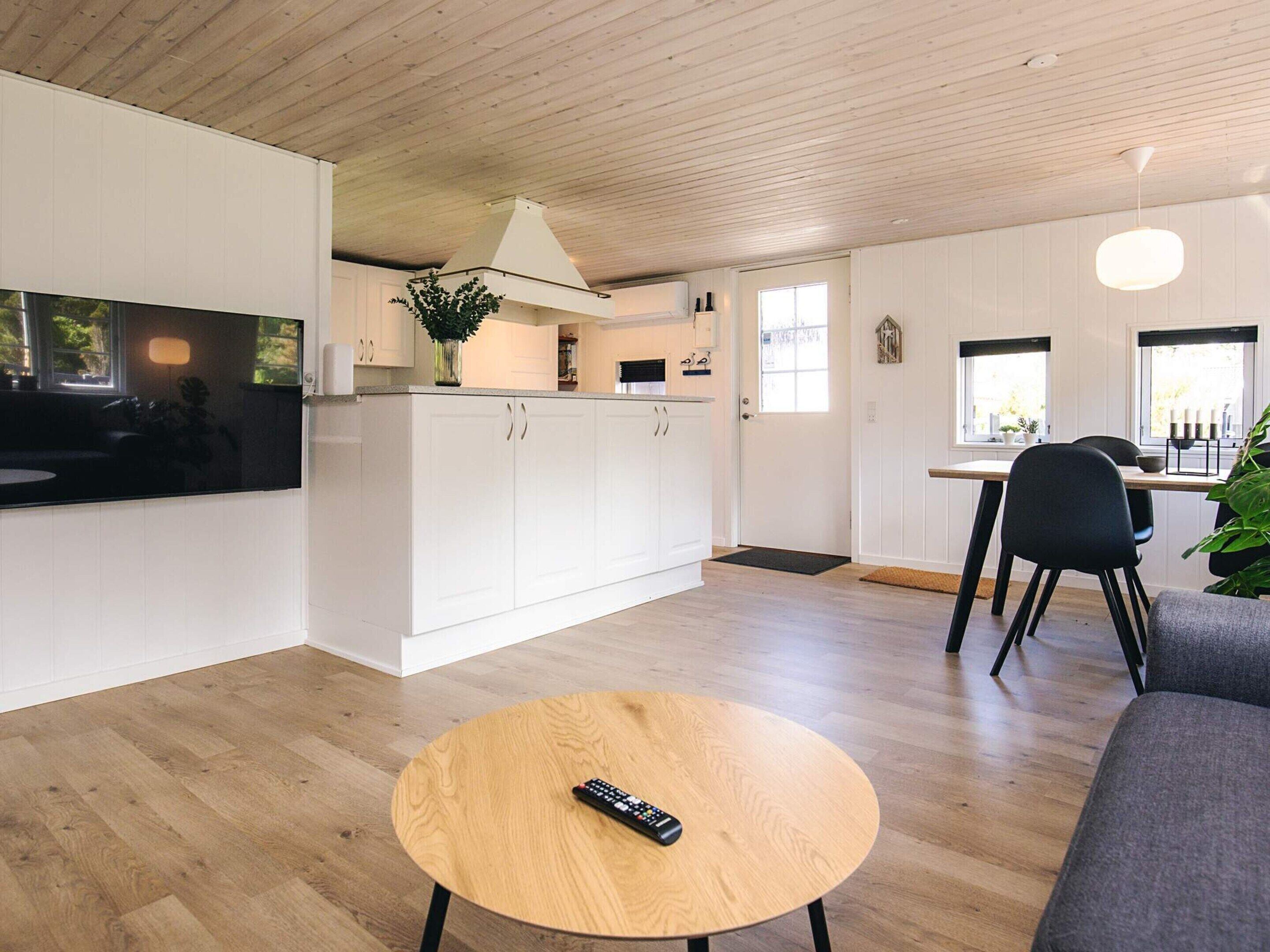 Eine moderne Küche mit weißen Schränken, einer Holzbalkendecke und einem Essbereich mit Tisch und Stühlen.