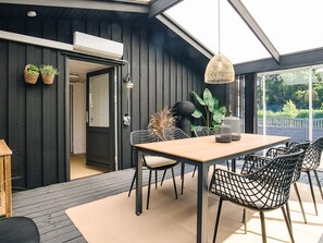 Un espace de restauration extérieur moderne, avec une table en bois et des chaises en fil de fer noir, entouré de plantes en pot et agrémenté d’un luminaire suspendu.