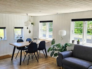 A dining area with a wooden table, four chairs, a sofa, and large windows with blinds. - 4 Star Holiday Home in Lokken (Lokken)