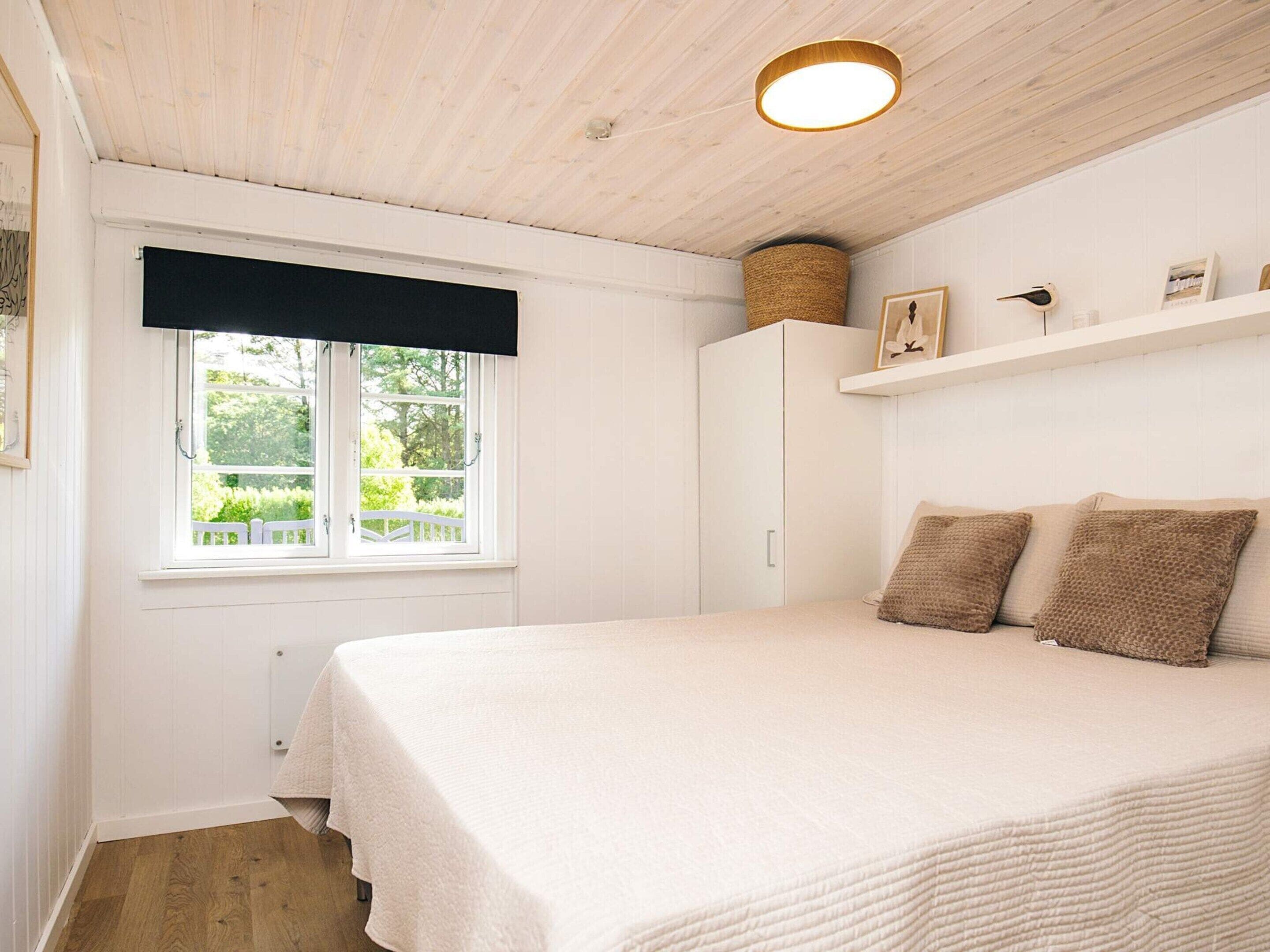 A bedroom with a bed, a window with a view, a white wardrobe, and a shelf with items.
