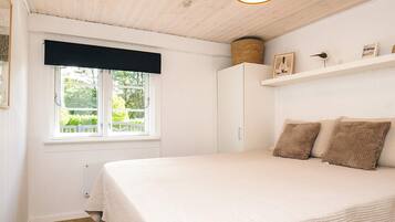 A bedroom with a bed, a window with a view, a white wardrobe, and a shelf with items.