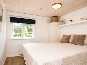 A bedroom with a bed, a window with a view, a white wardrobe, and a shelf with items. - 4 Star Holiday Home in Lokken (Lokken)