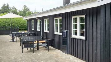 A building with a black exterior, white window frames, and a brick patio area with outdoor seating.