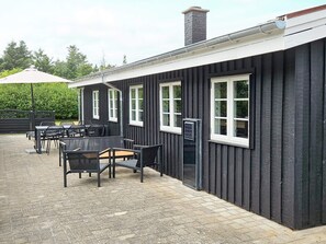 Un bâtiment à l’extérieur noir, avec des encadrements de fenêtres blancs et une terrasse en briques dotée de sièges extérieurs.