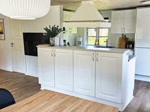 A kitchen with white cabinetry, a central island, a hanging light fixture, and a window with a view. - 4 Star Holiday Home in Lokken (Lokken)