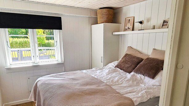 A bedroom with a bed, a window with a view, a wardrobe, and a shelf with items.