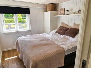 A bedroom with a bed, a window with a view, a wardrobe, and a shelf with items. - 4 Star Holiday Home in Lokken (Lokken)