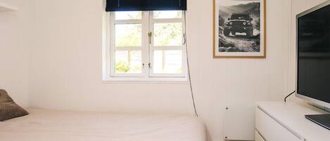 Un dormitorio con cama, ventana con persianas, radiador, televisión y un cuadro en la pared.