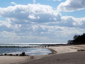 A beach with a rocky shoreline, a pier extending into the water, and a few people walking along the shore. - "country House" Modern Retreat (Kellenhusen)