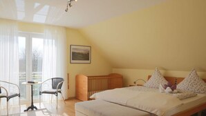 A bedroom with a large bed, a wooden headboard, a small table, two chairs, and a window with curtains. - "country House" Modern Retreat (Kellenhusen)