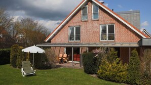A two-story brick house with a sloped roof, a covered patio with outdoor furniture, and a well-maintained lawn. - "country House" Modern Retreat (Kellenhusen)