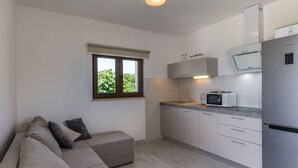 Eine kleine Küche mit integriertem Mikrowellenherd, einem Edelstahlkühlschrank und einem Fenster mit Blick auf Grünflächen.