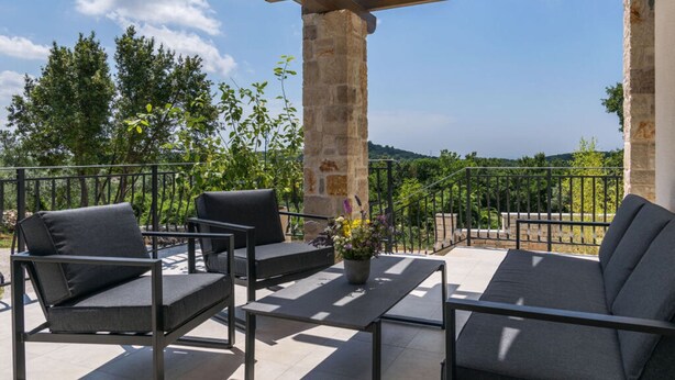 Eine Terrassenanlage im Freien mit einer Pergola, Steinsäulen und Blick auf die Landschaft.