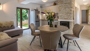 Ein modernes Wohnzimmer mit Kamin aus Stein, einem Essbereich mit rundem Tisch und einer Küche im Hintergrund.