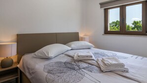 Ein ordentlich bezogenes Bett mit einem blattgemusterten Überwurf, zwei Kissen und gefalteten Handtüchern.
