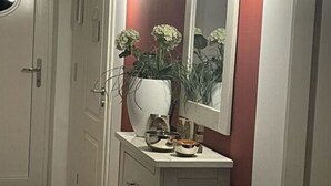 A narrow hallway with a white door, a white cabinet with a mirror, and a potted plant.