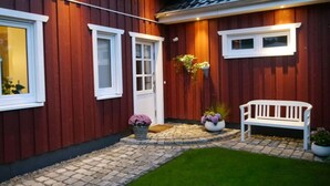 Una casa de madera roja con tejado de baldosas, un banco blanco y plantas en macetas.