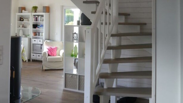 Una escalera con barandillas blancas y escalones de madera que sube a un nivel superior.