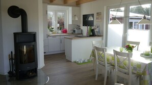 Una cocina moderna con estufa de leña, armarios blancos y un comedor con mesa y sillas.