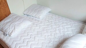 A single bed with a white quilted mattress and two pillows, a wooden headboard, and a plain wall. - 4 Person Holiday Home in Karrebaeksminde (Karrebæksminde)